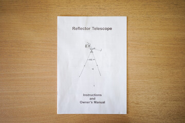 Instruction and owners manual book. Telescope parts on wooden table. Astronomy lesson exploring parts of telescope.