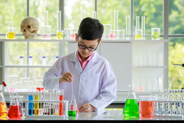 Serious Asian boy in lab coat and glasses with dropper and tube mixing colorful reagents while conducting scientific research in modern school laboratory