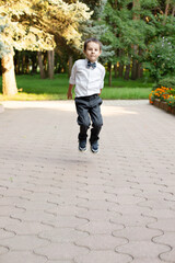 Fototapeta premium a beautiful little boy a schoolboy a first grader in a white shirt and gray trousers jumps
