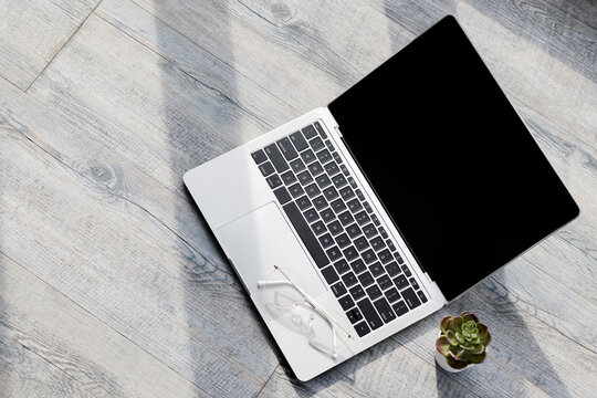 Closeup shot of Black blank screen monitor of silver laptop computer for advertisement ads and text copy space opened and placed on old wooden texture working table with green succulent plant pot