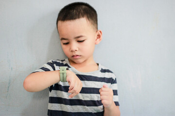 A cute boy wearing stylish shirt stay, looking at his smart watch touching the screen. A child using electronic device. Lifestyle concept.
