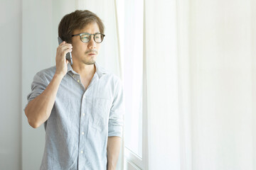 Asian businessman texting on smartphone standing next to window.