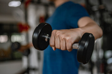 Training gym concept a young adult using his muscular strong arm lifting a dumbbell upward and downward in the gym
