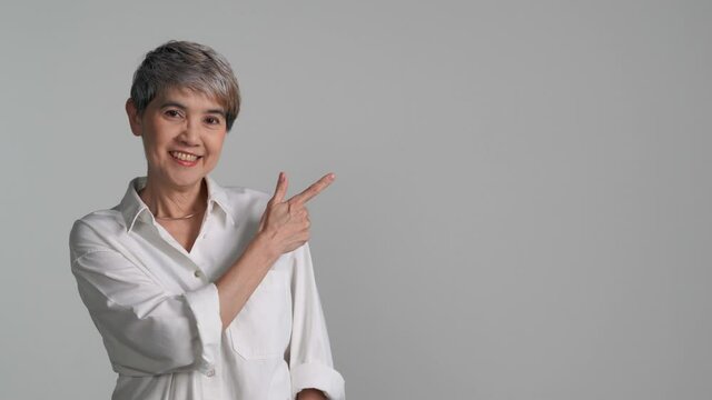 Middle aged Asian woman pointing fingers up at empty copy space for text isolated on white background