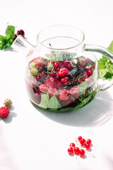 Tea with summer berries in a transparent teapot