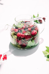 Tea with summer berries in a transparent teapot