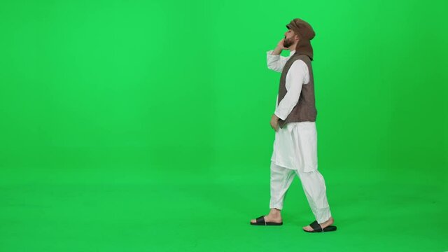 A man of Arab appearance in traditional clothes walking and talking on a mobile phone against the background of a chromakey, man uses smartphone.