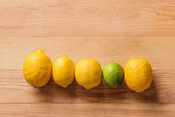 Fresh lime among lemons on wooden background. Concept of uniqueness
