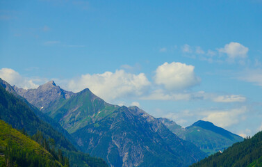 Panoramic view from Grubigstein, with rugged Zugspitze in background under blue sunny sky with cumulus clouds. Green valley at the foot of majestic alpine mountains, in Lermoos, Tyrol