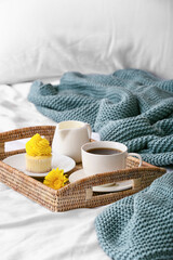 Tray with cup of coffee, cupcake and milk on bed