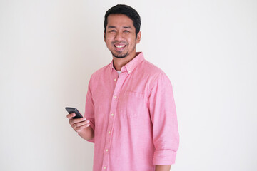 Attractive Asian man wearing pink shirt smiling confident while holding his smartphone