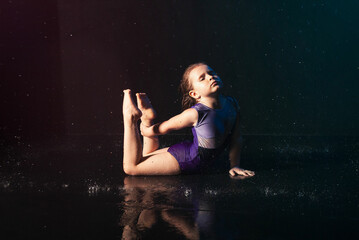 a little charming cute girl gymnast in the water on a black background in the aqua studio does...