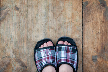 Person wearing house slippers stands on weathered wooden floor