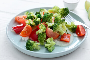 Plate of tasty salad with broccoli on light wooden background, closeup