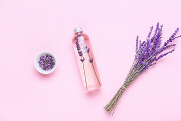 Bottle of lavender essential oil and flowers on color background
