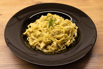 Chicken tagliatelle pasta with delicious italian pesto sauce on wooden background