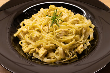 Chicken tagliatelle pasta with delicious italian pesto sauce on wooden background