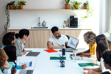 Indian boss shows business evolution graphs to multiracial employees in bright spacious office. Copy space.