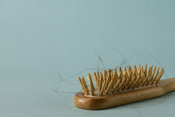 A wooden hairbrush with hair on light blue background with copy space, close-up