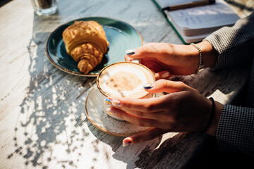Cappuccino and croissant on the table in the cafe. The morning sunlight falls on the table, beautiful shadows appear.