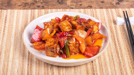 Serving of hot sweet and sour tofu with onions and peppers in a plate with chopsticks, close-up
