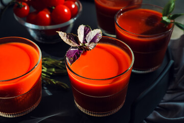 Glasses of tasty tomato juice on dark background