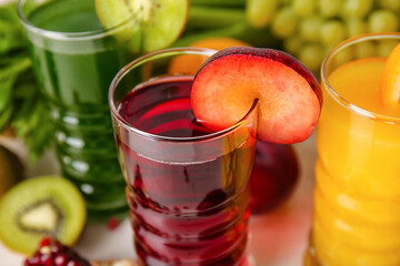 Glasses with healthy juice, fruits and vegetables on light background