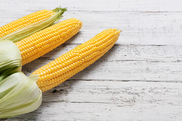Fresh corn cobs on light wooden background