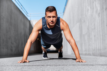 Naklejka premium fitness, sport and training concept - young man doing push ups on city street