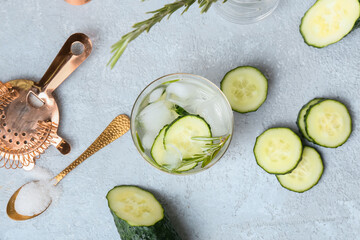 Glass of cold gin tonic and cucumber slices on light background