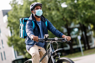 food shipping, health and people concept - indian delivery man in bike helmet and mask with thermal insulated bag and smatphone riding bicycle on city street