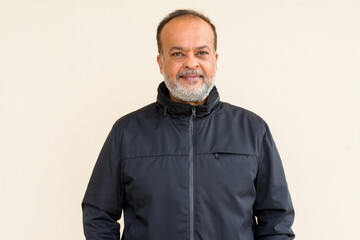 Portrait of happy bearded Indian man smiling against plain wall