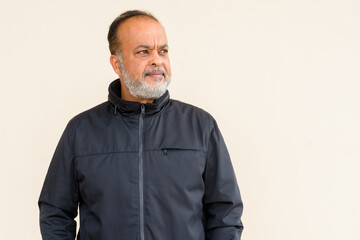 Portrait of handsome bearded Indian man thinking against plain wall