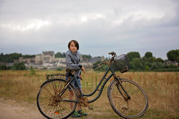 Fototapeta na wymiar Beautiful preteen boy, child, standing next to an old bicycle in front of Amboise town in France