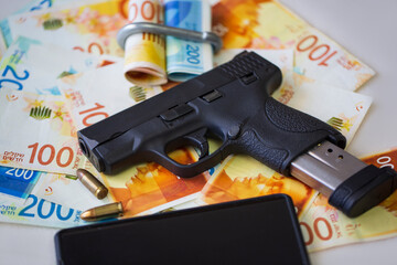 Black gun pistol with ammunition and mobile phone on on stack money Israeli New Shekels banknotes...