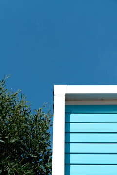 Minimalist picture of the corner of a mobile home in front of blue sky with olive tree