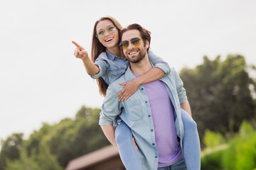 Fototapeta premium Photo of cheerful good mood smiling couple relaxing together outdoors man hold woman piggyback point finger sightseeing