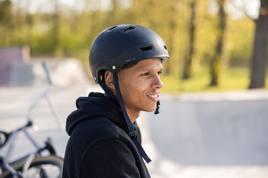 A cyclist sits on a ramp in a park on a spring afternoon with a helmet on his head and looks forward at the ramp wondering if he can pull off a new trick