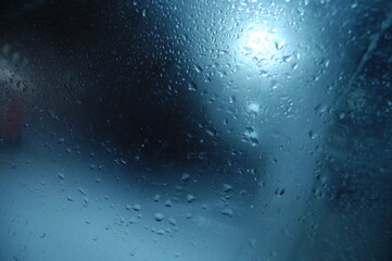 Drops Of Rain On Blue Glass Background. Street Bokeh Light Out O