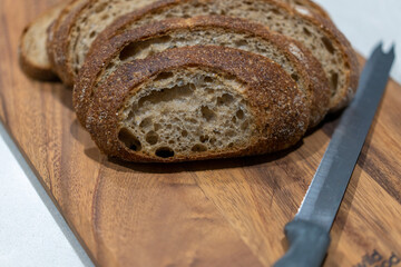 Fresh sliced bread on wooden board with knife in kitchen