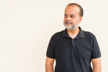 Portrait of handsome bearded Indian man thinking against plain wall