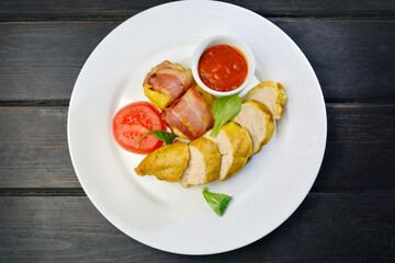 baked potato wrapped in bacon with chicken breast with sauce on