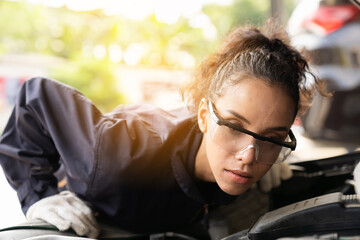Obraz premium Female mechanic working at the garage. Professional female car mechanic examining, repair and maintenance under hood of car at auto car repair service. Car service and Maintenance concept