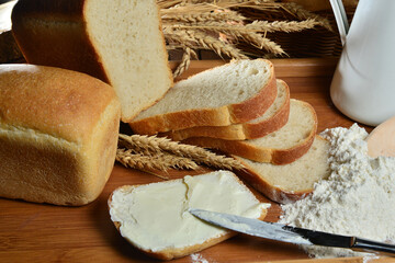 Fresh sliced bread with butter and milk jug on wooden board with