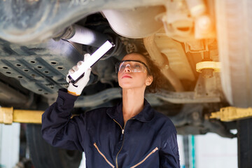 Female worker working and using wrench tool for maintenance car engine underneath lifted car. Female mechanic vehicle service maintenance checking under car condition in garage