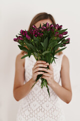 Faceless portrait of a young woman in white dress holding fresh flowers bouquet. Alstroemeria flowers