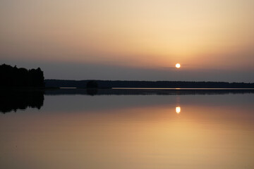 Quiet evening after a sultry day. Beautiful sunset over the lake. Reflection and horizon. Evening dim soft sun
