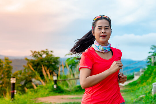 Half-body image of a female trail runner wearing a pink runner, sportswear, practicing on a dirt road on a high mountain with a happy mood, on a clear day Behind is a mountain view.