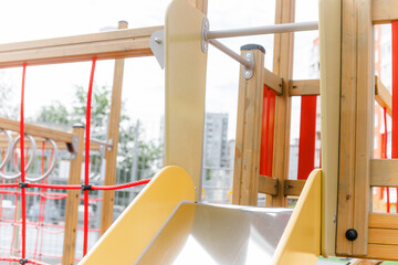 An outdoor colorful playground next to the house. A summer day. Children's playground with rubber floor covering. Close-up, details of a wooden house for children. Metal slide.