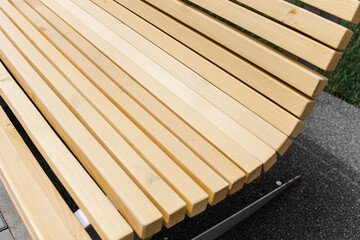 A new wooden bench with metal legs on the street. A summer day. Outdoor colorful playground with rubber flooring next to the house.